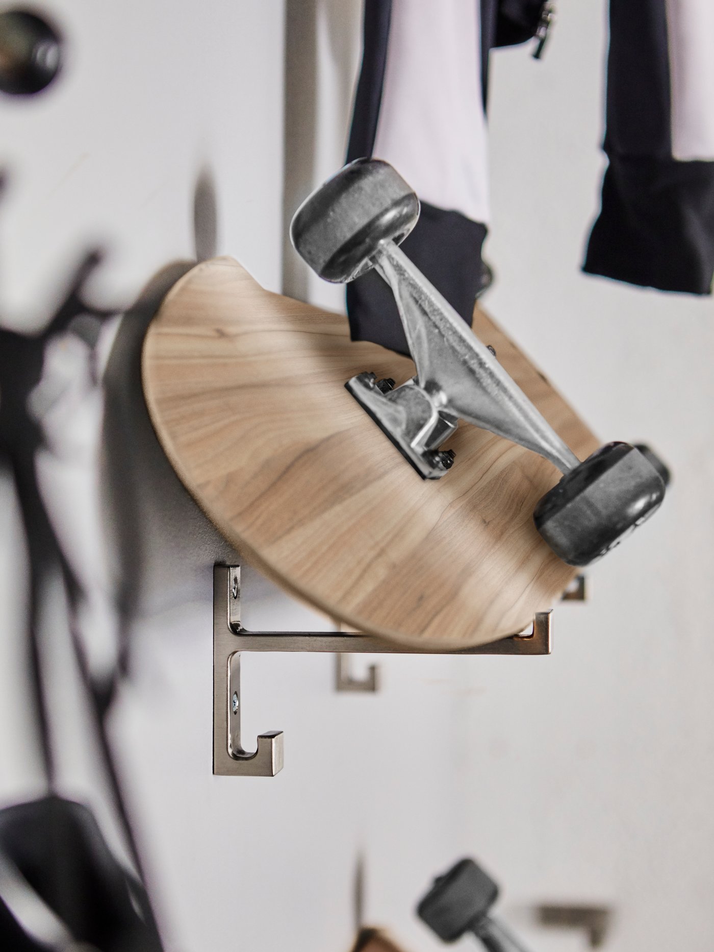 Un skate apoyado contra la pared con dos ganchos BJÄRNUM de aluminio.