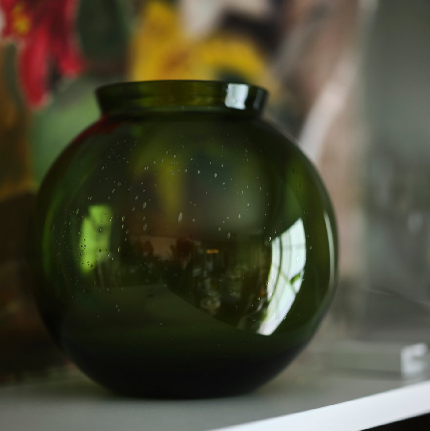 A green KONSTFULL vase on a white shelf.