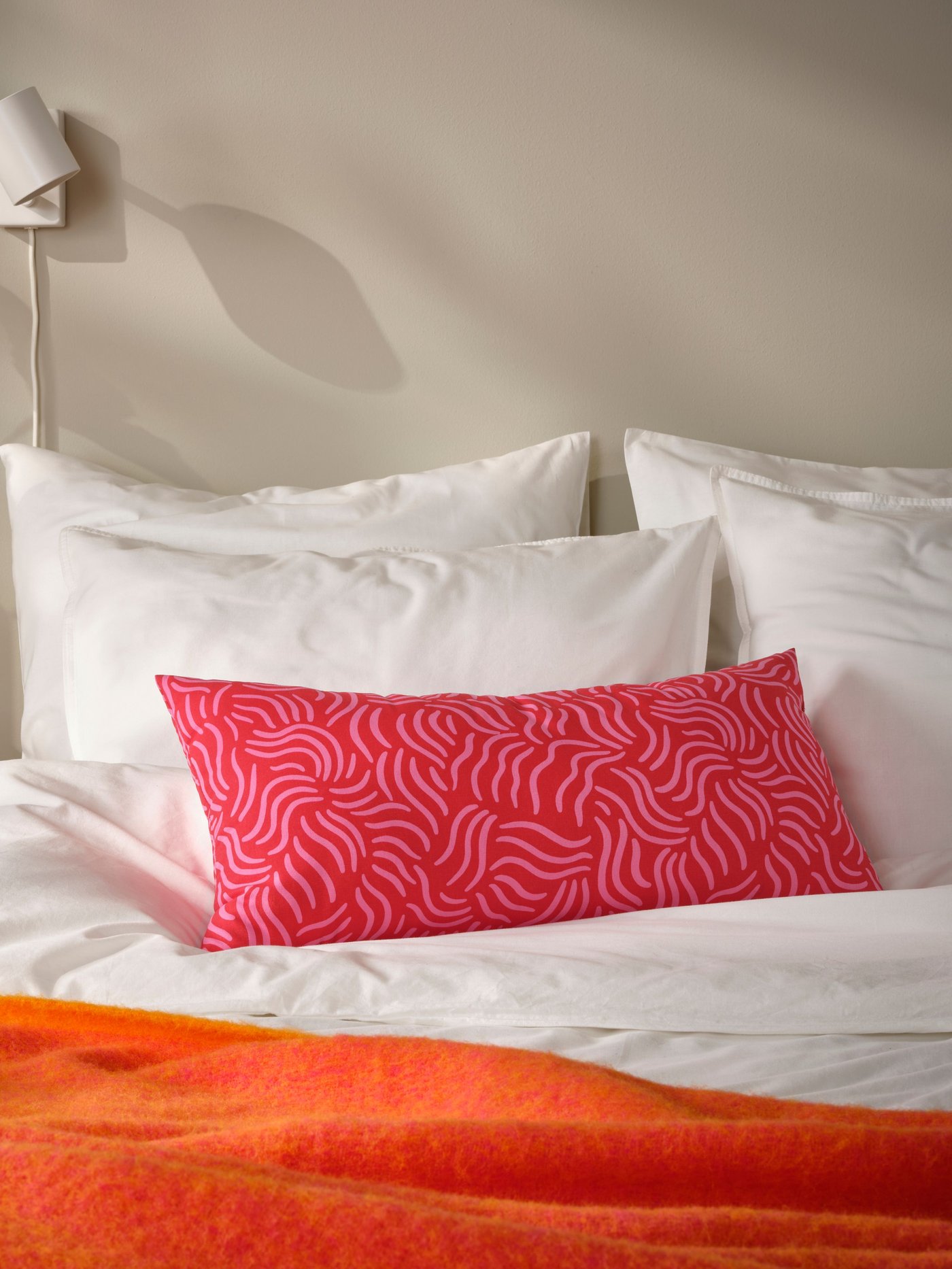 A bright red/bright pink SANDMOTT cushion in the bedroom
