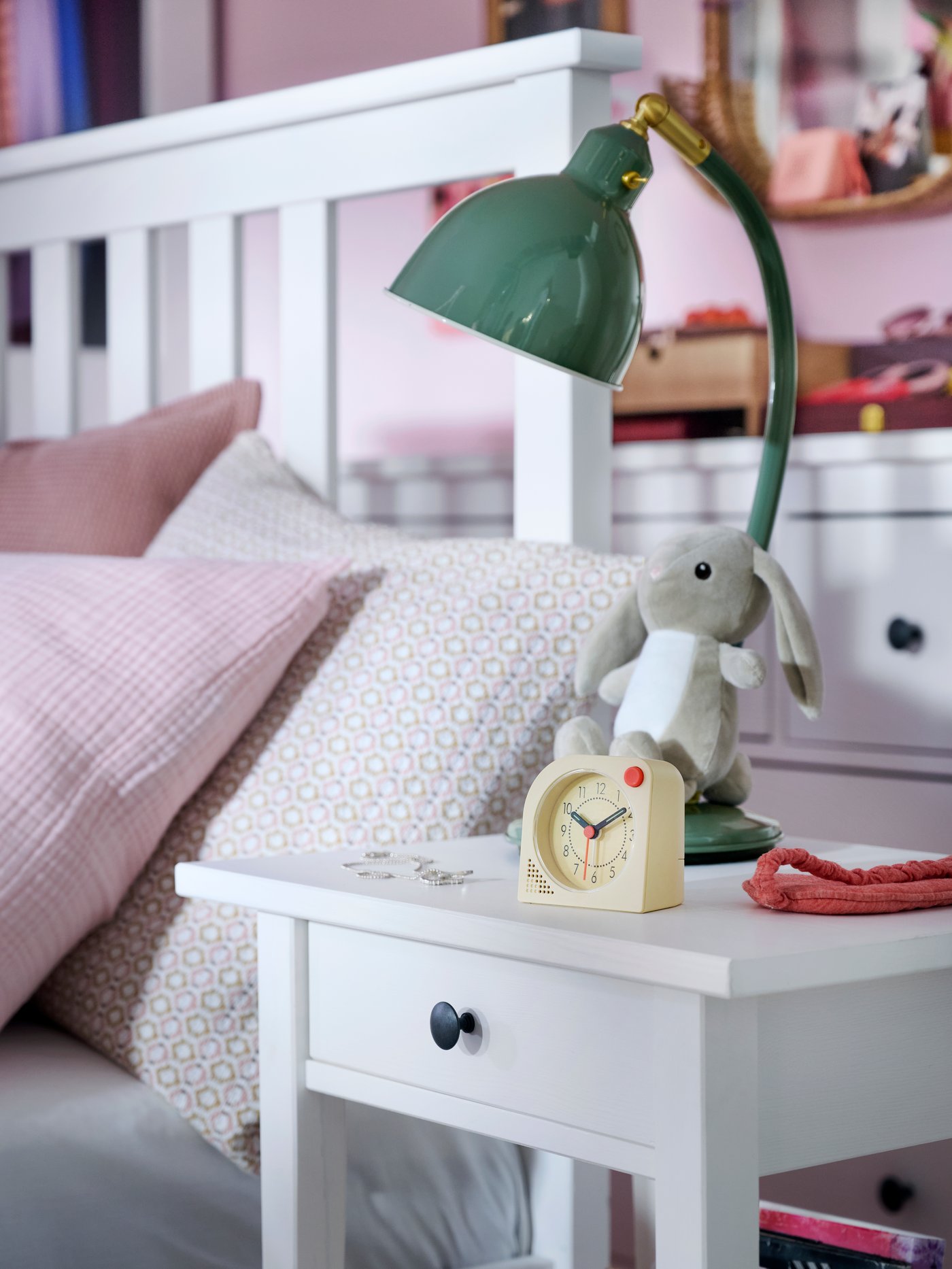 Close-up of HEMNES bedside table with TJINGA alarm clock, DVÄRGHARE soft toy rabbit and RÖDFLIK desk lamp.