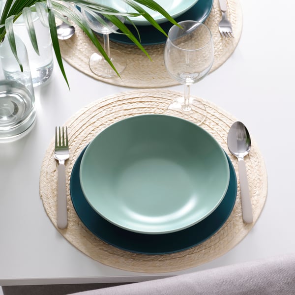 Un set de platos FÄRGKLAR verde sobre un individual de fibra. 