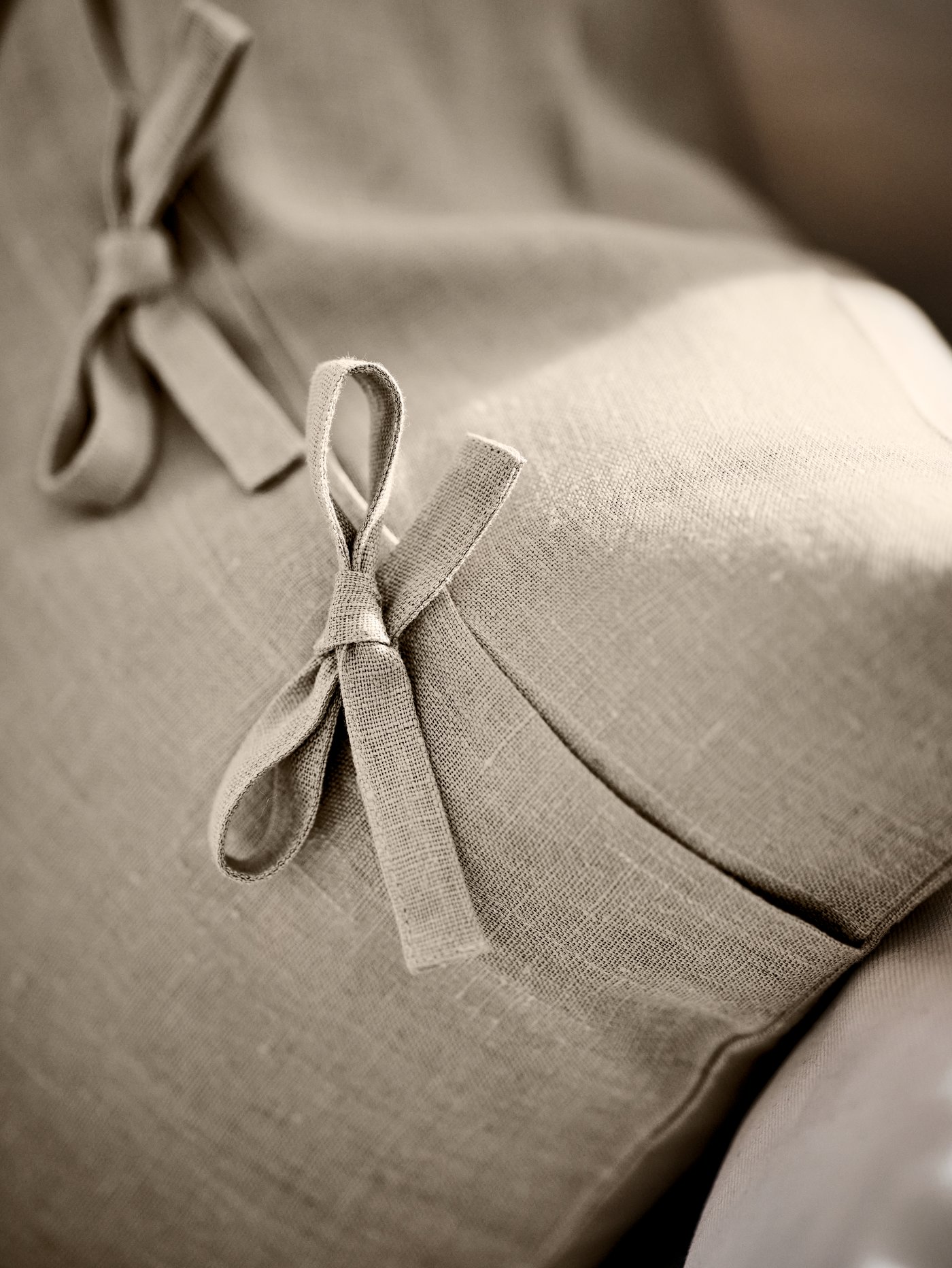 The back of a beige AINA cushion on a cream sofa, showing two of the fastenings tied in bows.