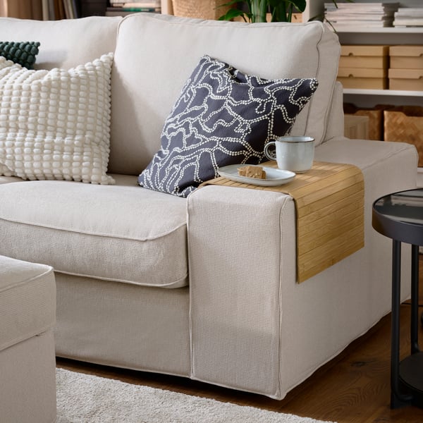 A light beige KIVIK corner sofa, featuring textured cushions and a wooden side table, elegantly styled in a living room setting.