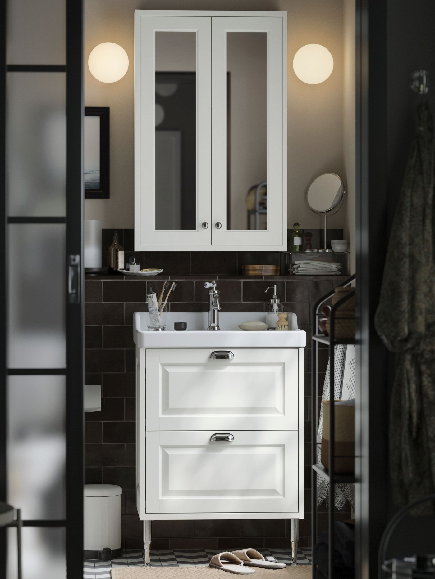 A small traditional-style bathroom with white TÄNNFORSEN storage furniture, round lamps and black details.