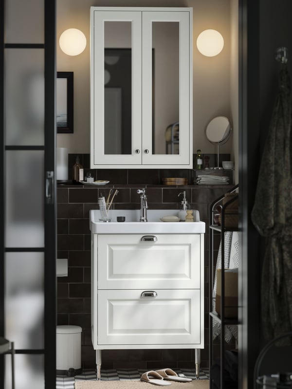 A small traditional-style bathroom with white TÄNNFORSEN storage furniture, round lamps and black details.