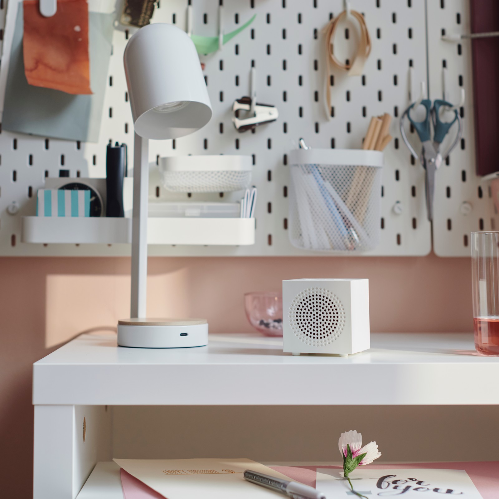 A white KALLSUP portable Bluetooth speaker stands on a LÄNGDHOPP pull-out desk next to an ENSMÄRKE desk lamp.