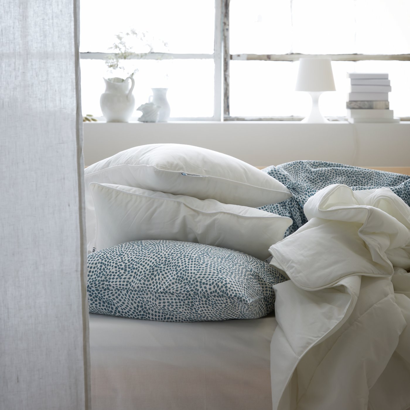 Différents oreillers, coussins et couettes sur un lit.