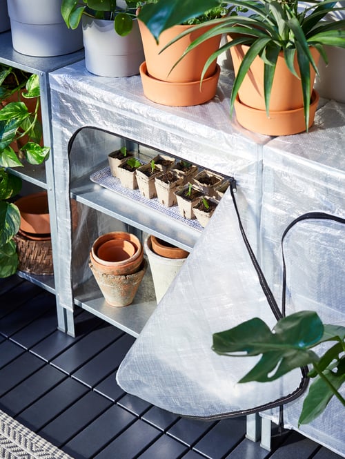 A steel HYLLIS shelving unit has potted plants on top and a zippered cover open to show empty pots and small seedlings.