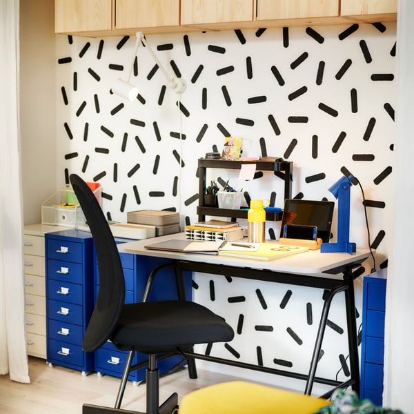 A workspace in a bright, colourful room with a GLADHÖJDEN sit-stand desk placed by a graphic-patterned wall.