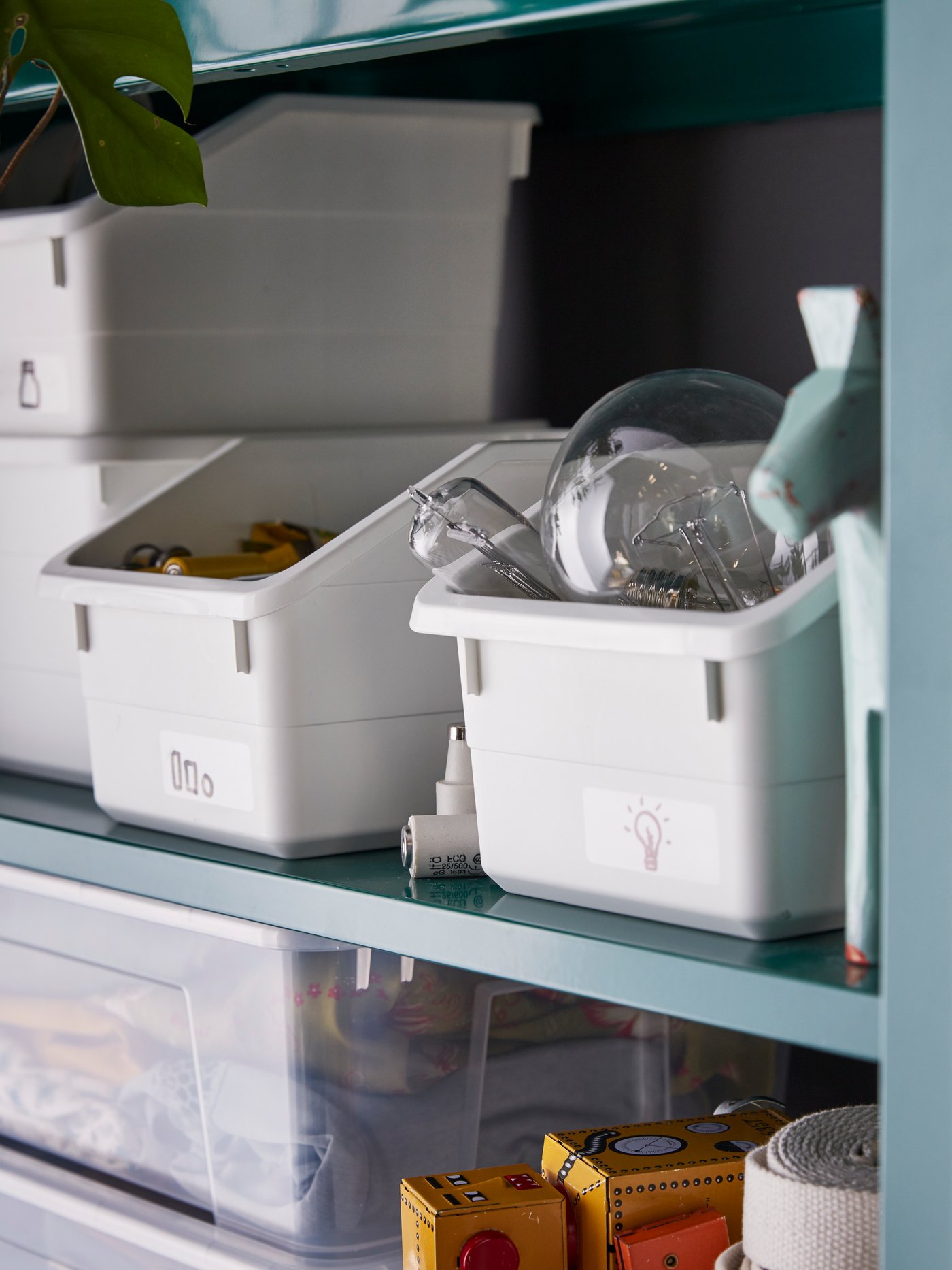Shelves are holding open, white SOCKERBIT boxes filled with light bulbs and batteries nearby stacked transparent SAMLA boxes.