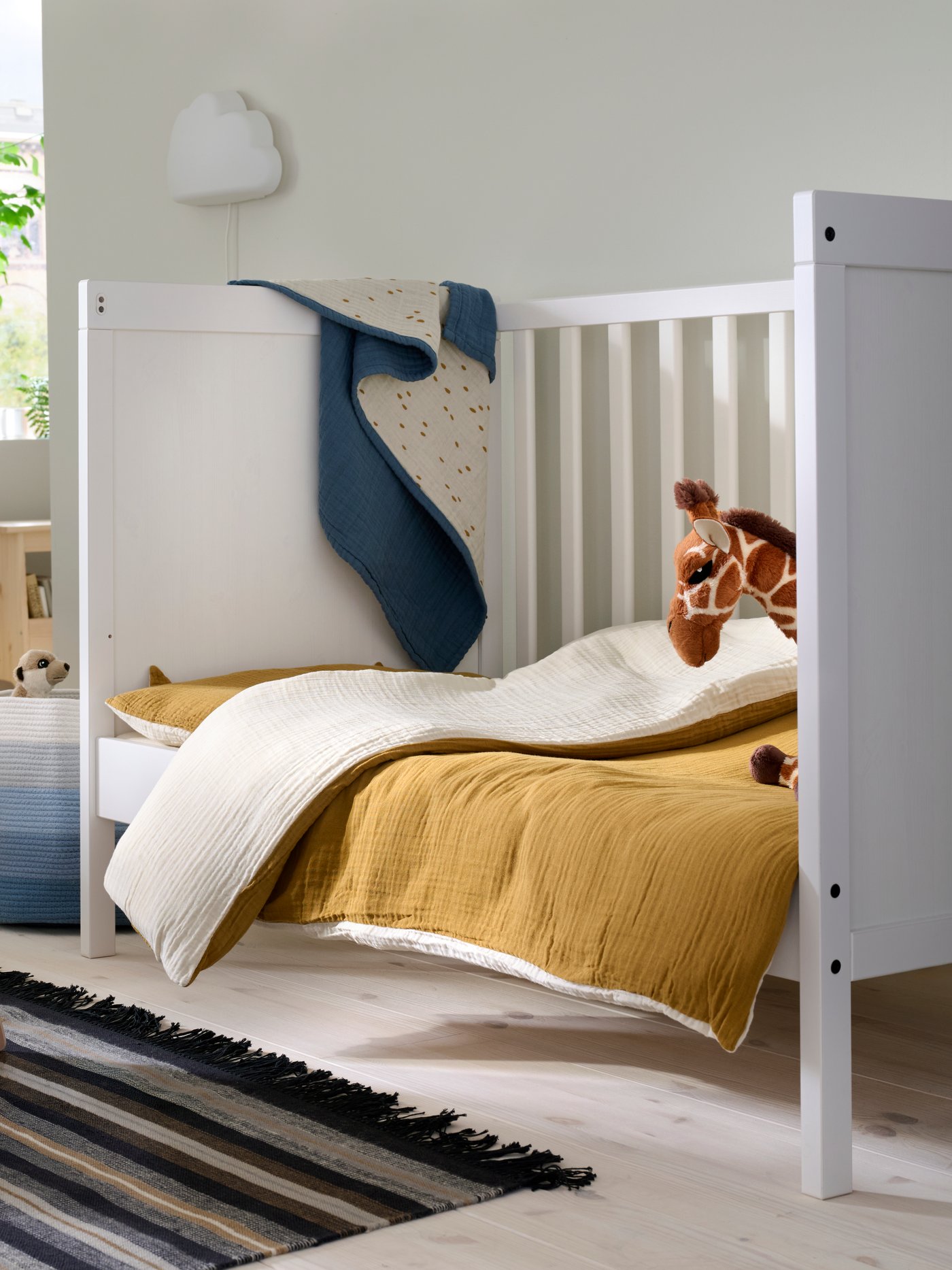A child’s SUNDVIK cot in a family bedroom with a brown quilt and a giraffe toy.