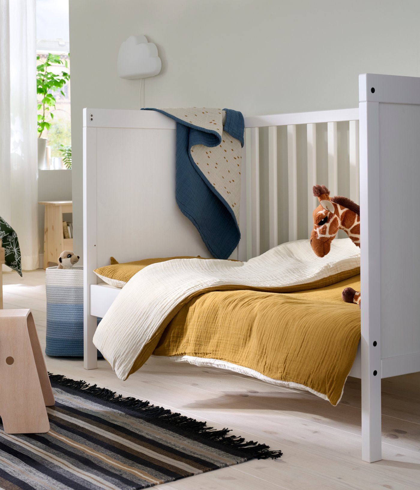 A child’s SUNDVIK cot in a family bedroom with a brown quilt and a giraffe toy.
