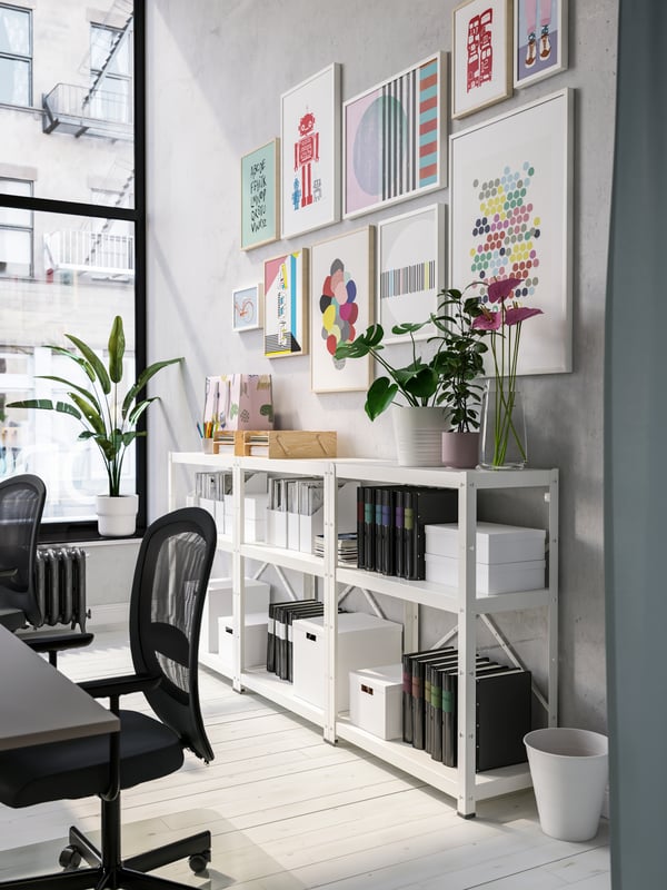 White shelving units with black folders and white boxes, colorful framed art on the wall, black office chairs.