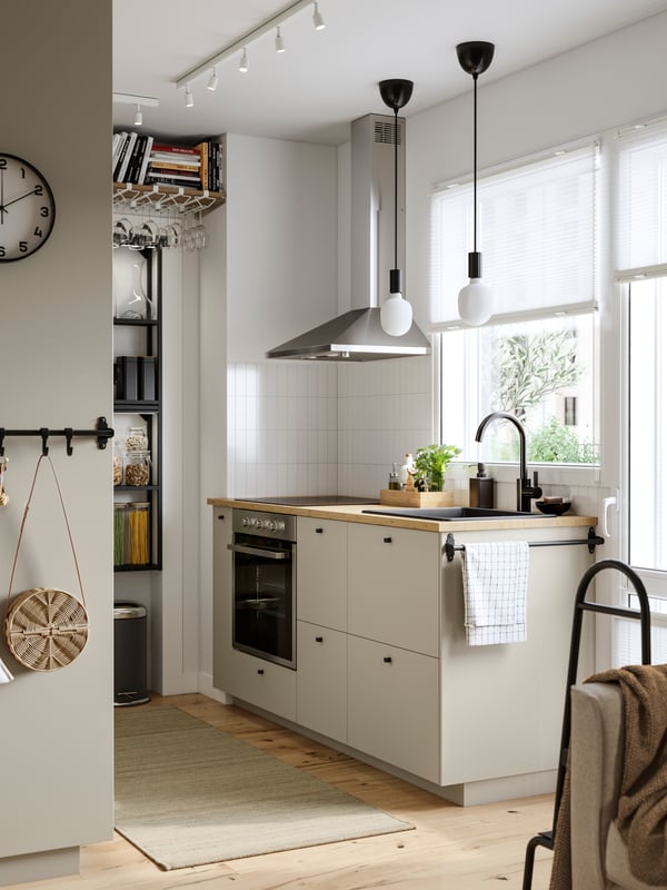 A kitchen has cabinets with beige HAVSTORP fronts, an ENHET wall frame with shelves in anthracite and a rug on the floor.