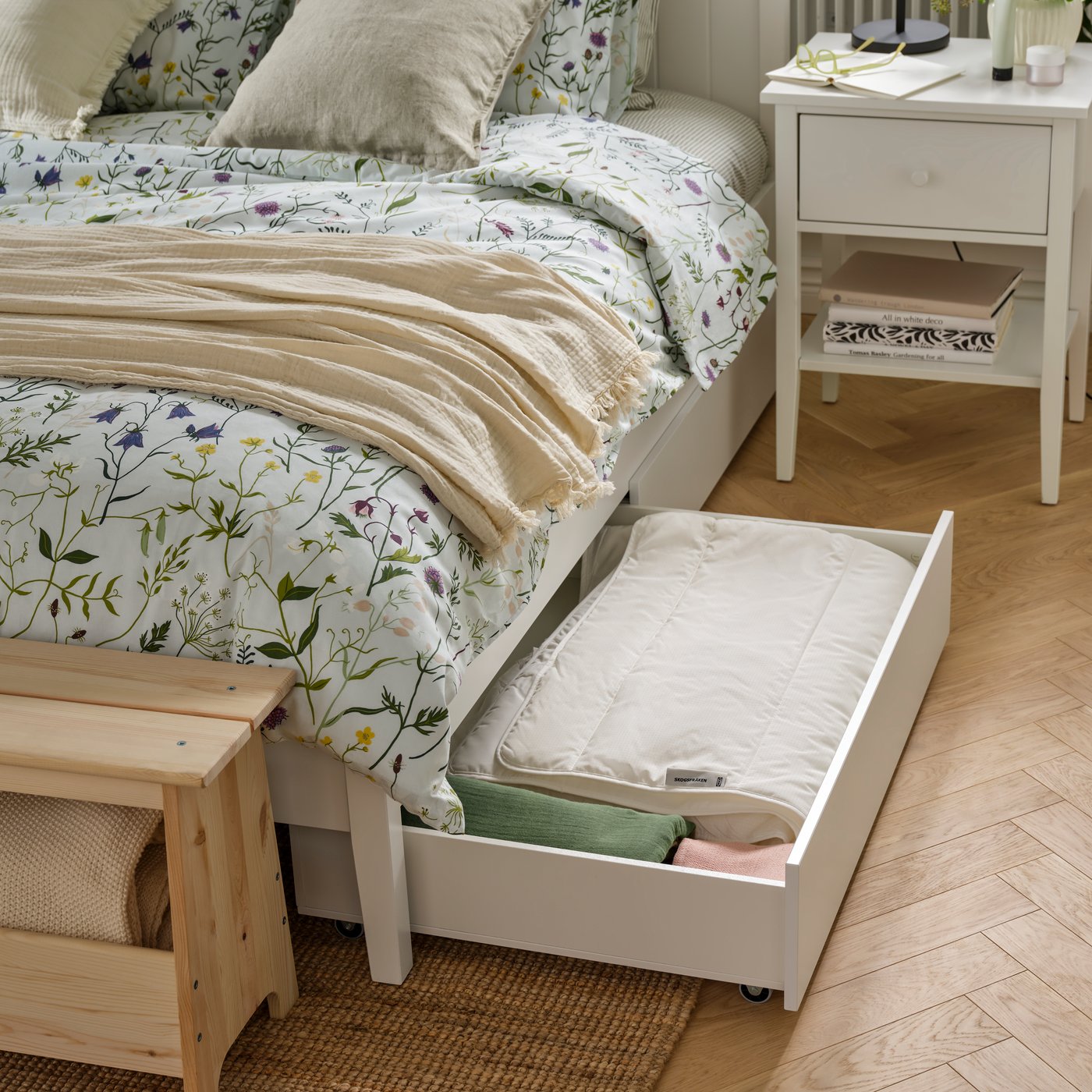 A bedroom featuring a white GULLABERG bed frame with four storage boxes, complemented by floral bedding and a bedside table.