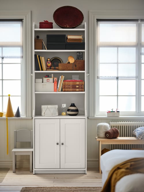 Un salon dans lequel on retrouve une armoire haute blanche à deux portes, un banc en bois et une chaise pour enfants grise.