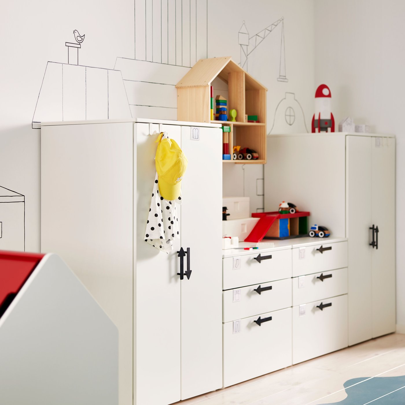 White SMÅSTAD/PLATSA storage units with JÄRNSPARV black handles against a wall with a FLISAT doll’s house/shelf on it.