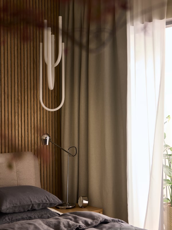 The corner of a bedroom by a window that has ANNAKAJSA room-darkening curtains and ROSENROBINIA sheer curtains hanging on it.