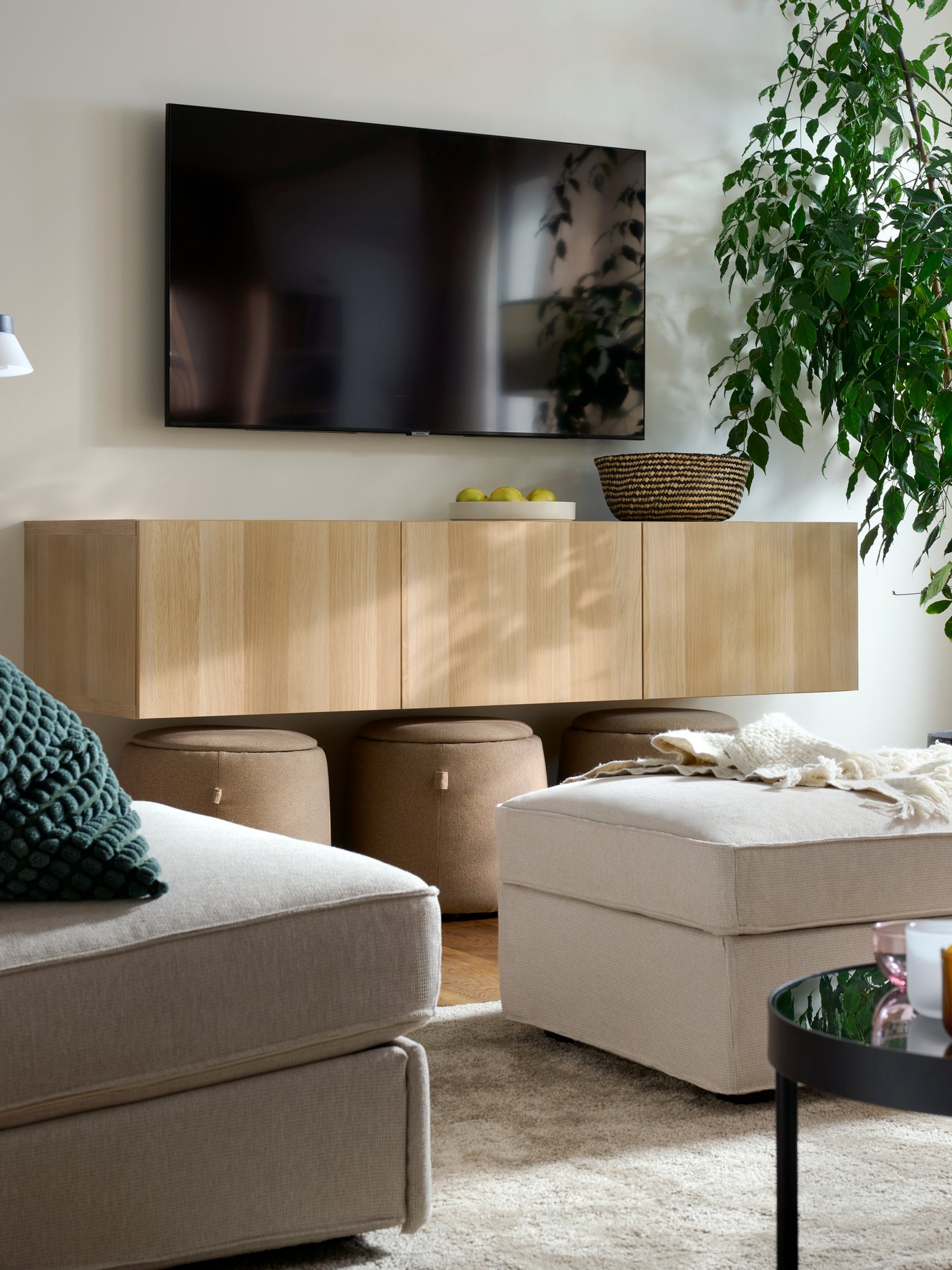 A light, bright living room with a combination of KIVIK seating, a STOENSE rug, a wall-hung TV and a big, leafy plant.
