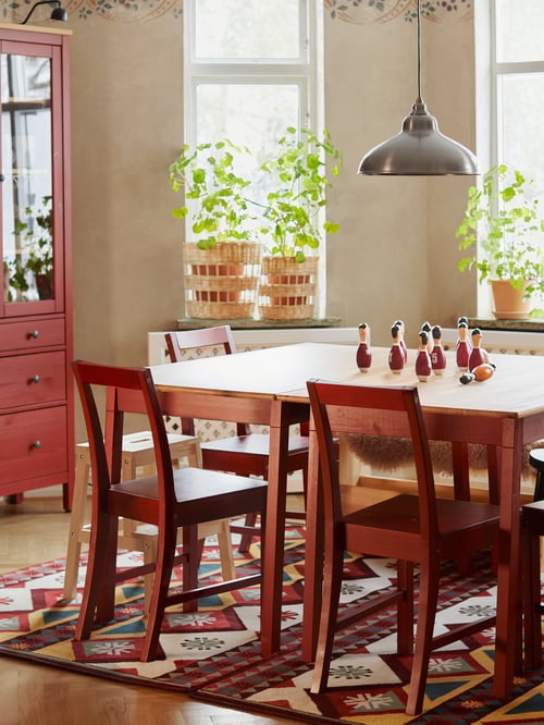 Kitchen area featuring multiple red chairs set at a rectangular table, a glass door cabinet, a rug. and a pendant lamp.