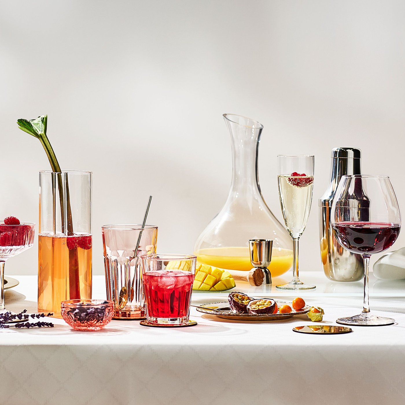 A STORSINT carafe with juice, a STORSINT red wine glass and several pink POKAL glasses are placed on a white tablecloth.