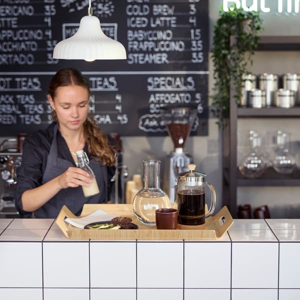 Café scene with a barista preparing  a bamboo SILVERHAJMAL tray to serve drinks and food on a tiled café counter.