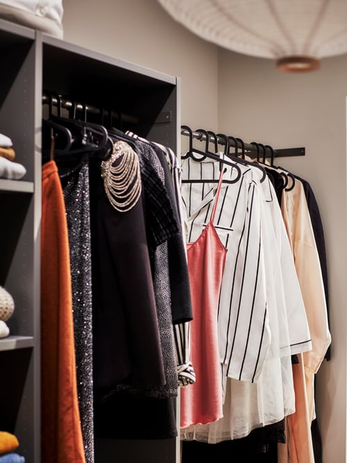 Une combinaison d'armoire gris foncé en bois sans portes, des vêtements sur des cintres et une suspension blanche en forme d’oignon.