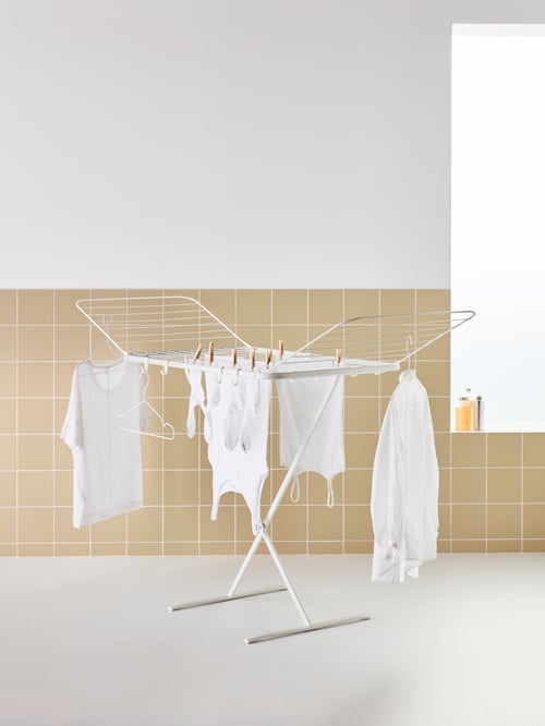 Des vêtements sont suspendus à des pinces et à des cintres sur un séchoir d’intérieur et d’extérieur MULIG en acier à revêtement blanc, dont les deux ailes sont déployées.