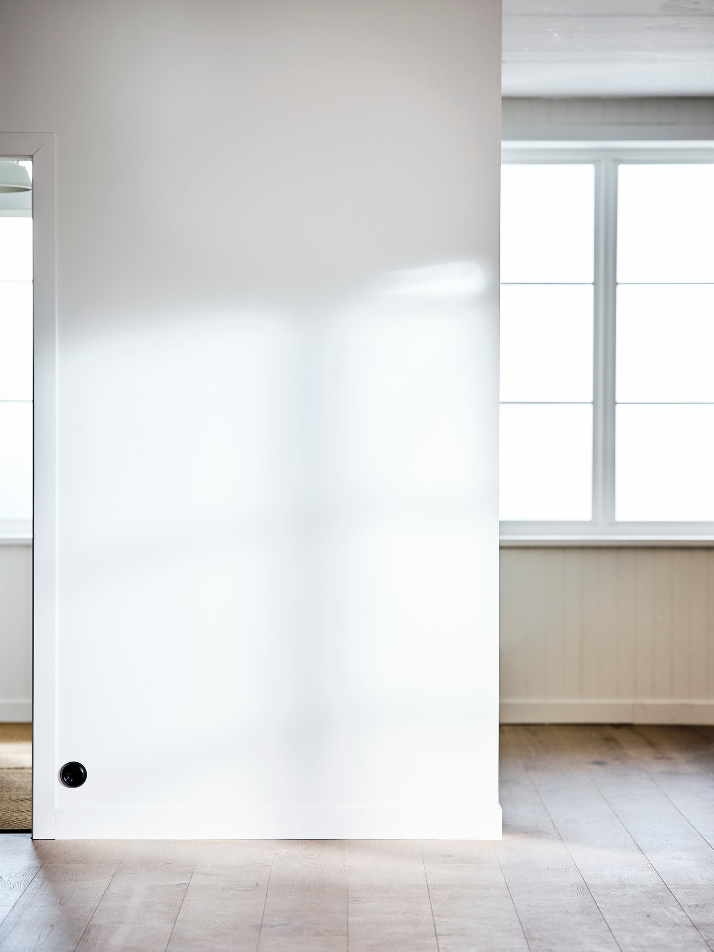 Ein leeres Zimmer mit grossen Fenstern, weiss gestrichenen Wänden und weiss lasierten Holzböden.