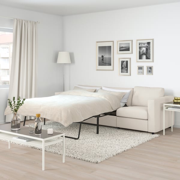 En vimle 3 seter sovesofa i beige farge i en stue med lys gulvteppe. 