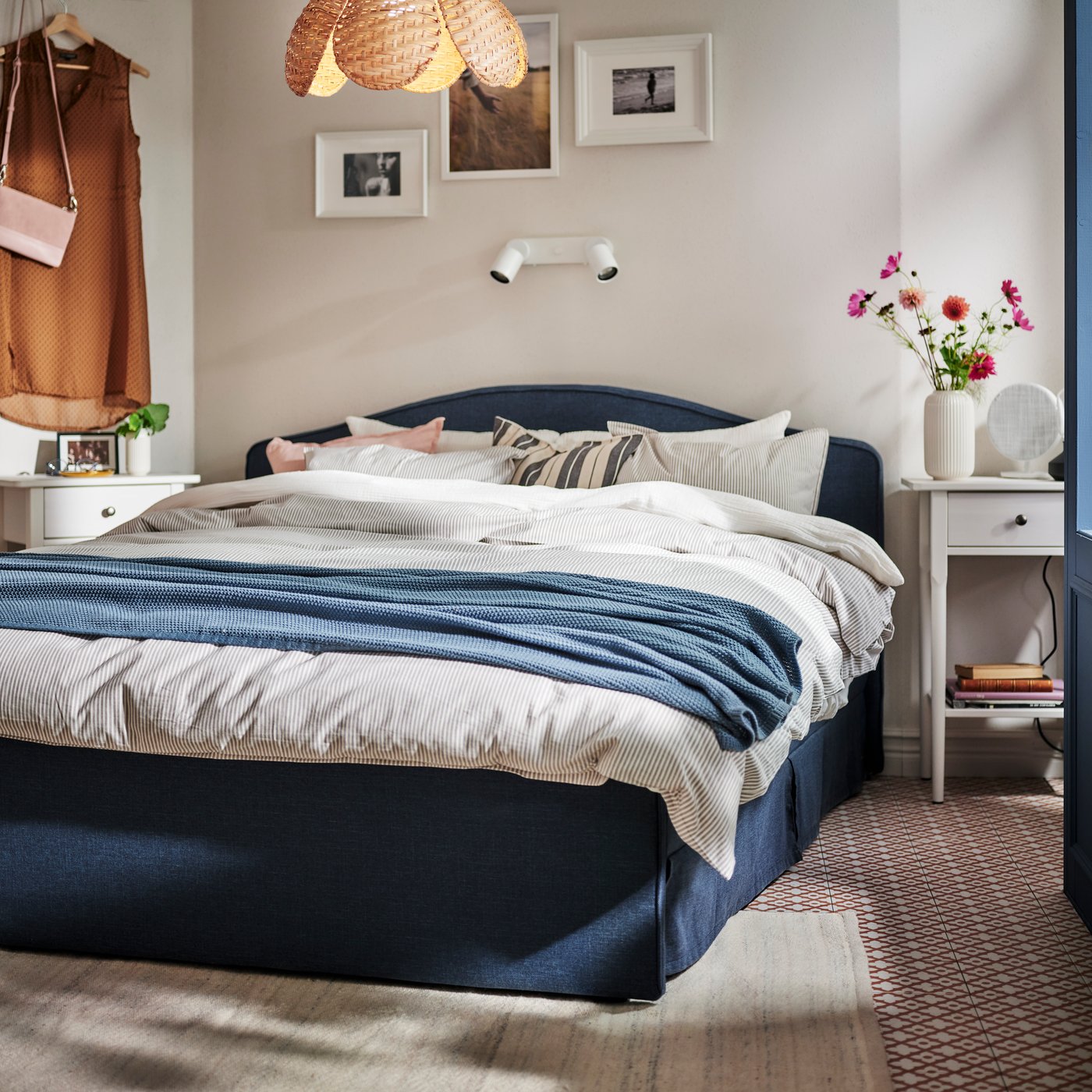 A blue grey HUMLEMOTT throw lies across a RAMNEFJÄLL upholstered bed that’s covered in SCHERSMIN and SOLFIBBLA bed linen.