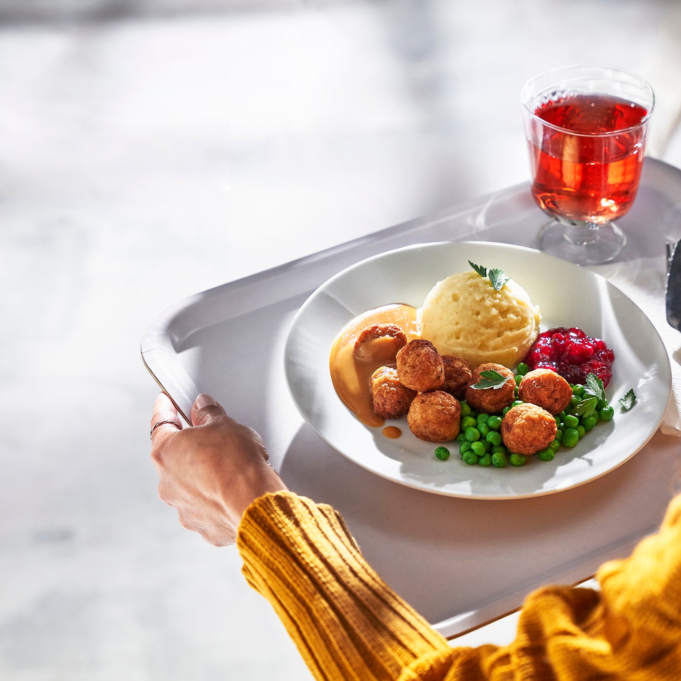 Una vista dell'alto di una persone che ha tra le mani un vassoio con polpette di pollo, vari contorni e una bevanda.