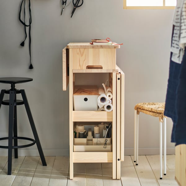Grey wall, wooden floor, RESARÖ mobile drop-leaf table with storage in pine, stools on both sides.