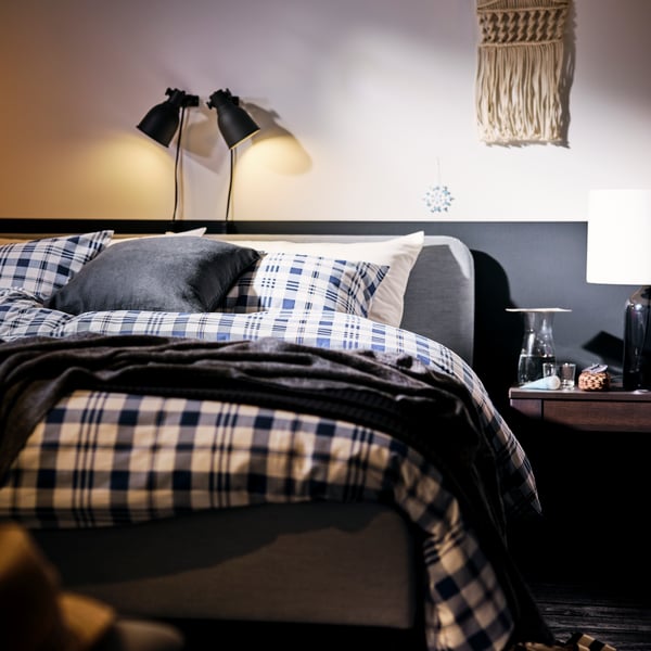 A bedroom with a HEKTAR wall spotlight that provides lighting while reading in bed.