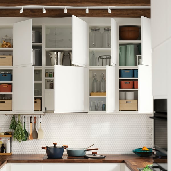 Wall-mounted kitchen cabinets have matt white VOXTORP doors and some of them have been opened, showing items stored inside.
