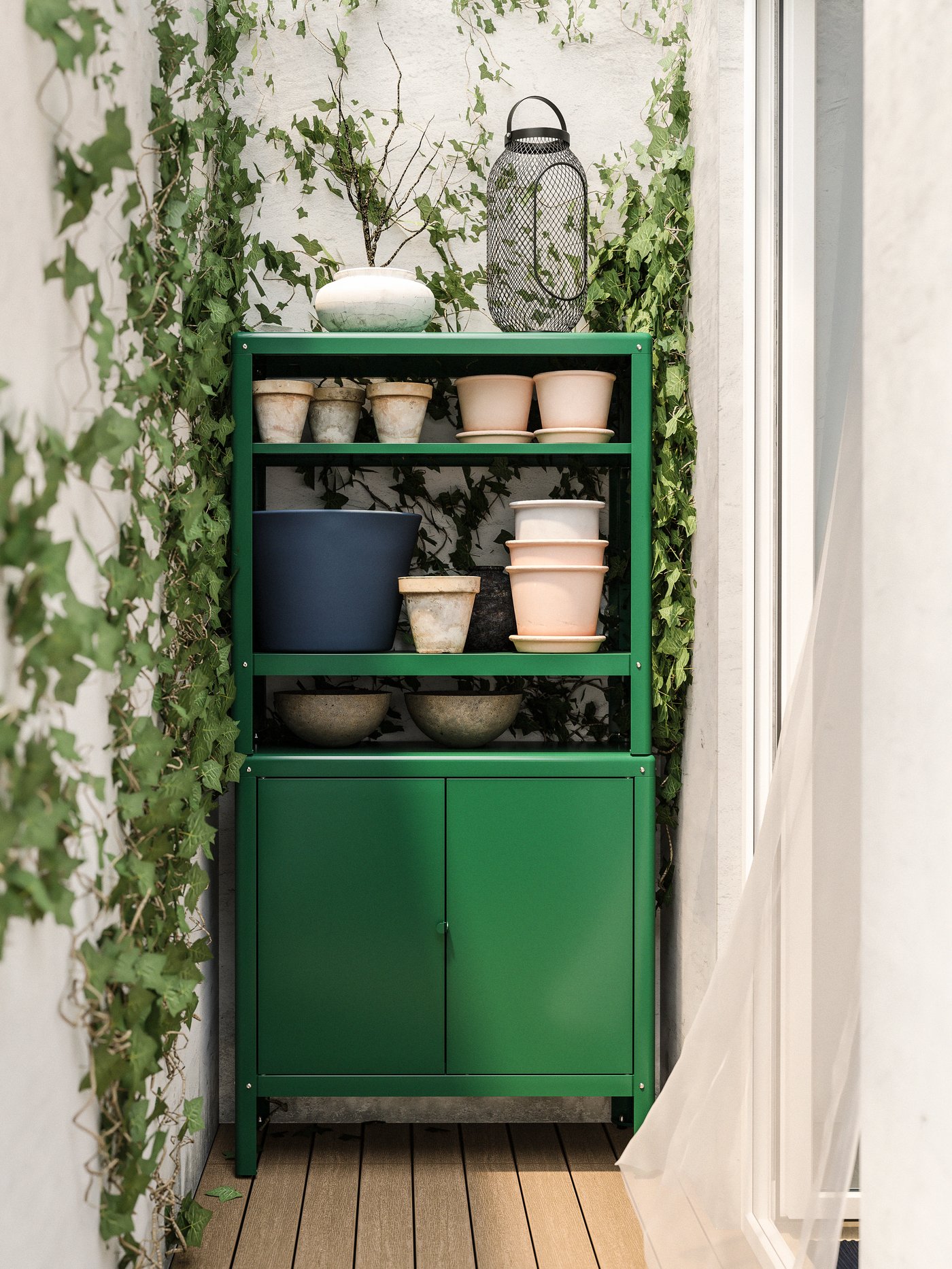 Ein grüner Schrank vor einer Wand mit Efeu und mit Übertöpfen auf den Ablagen.