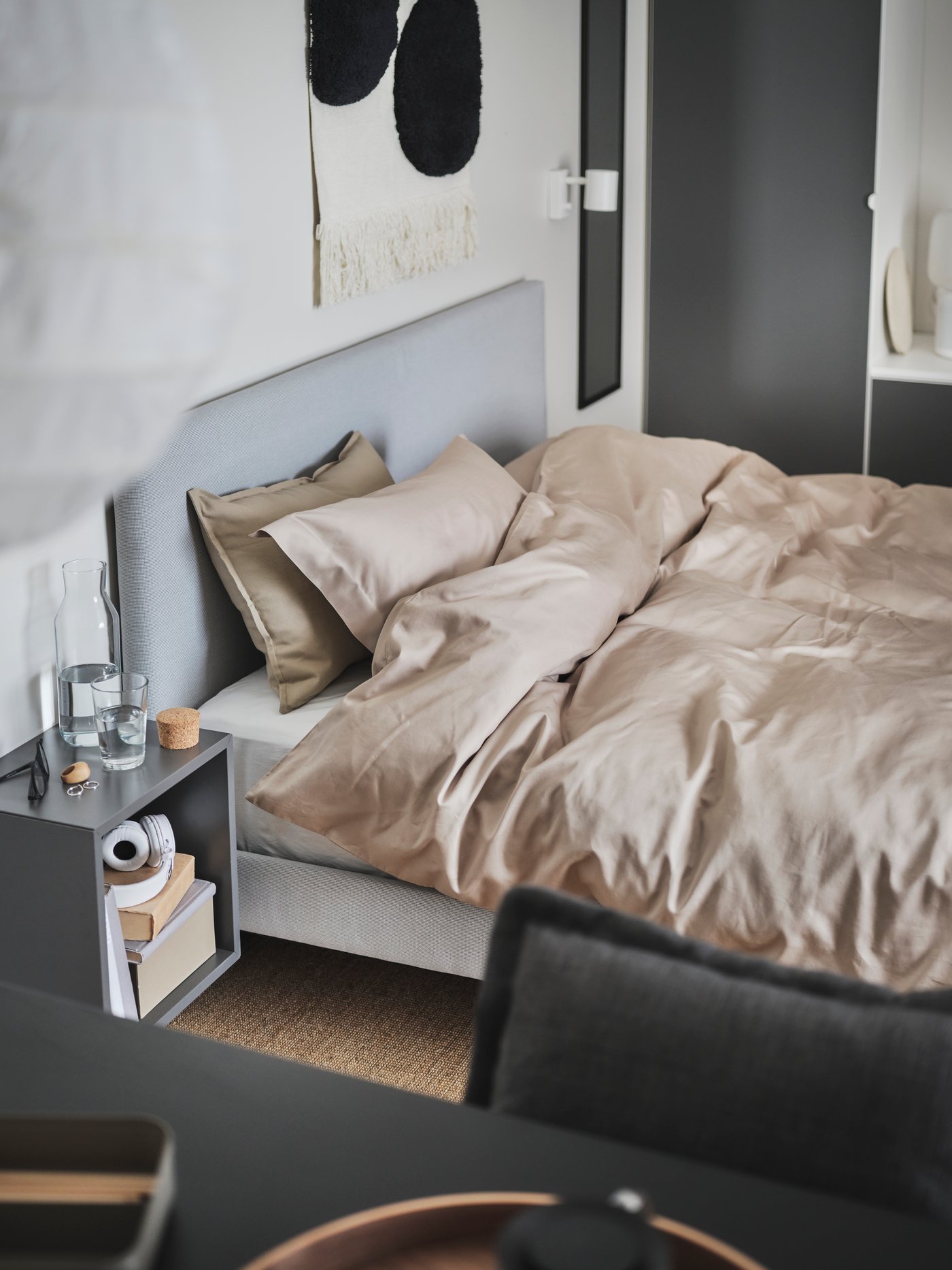 Es ist ein hellgraues gepolstertes GLADSTAD Bettgestell mit gepolsterten Bettkästen zu sehen, das vor einem grauen Kleiderschrank steht.