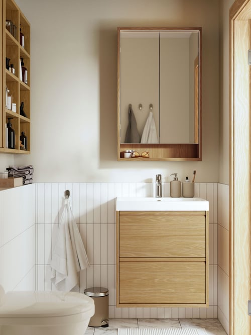 A bathroom featuring an ÄNGSJÖN wash stand with drawers, a mirror, a toothbrush holder, a hanging towel, and a trash can.