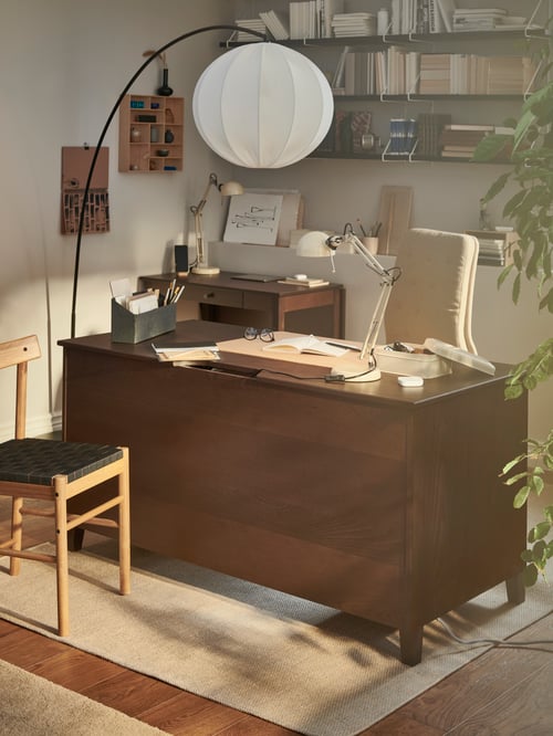 A IDANÄS desk with a conference chair, a floor lamp, and a flatwoven rug on the floor. In front of it, a NACKANÄS chair.