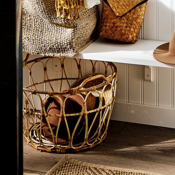 A SNIDAD basket stands under a bench in a hall.
