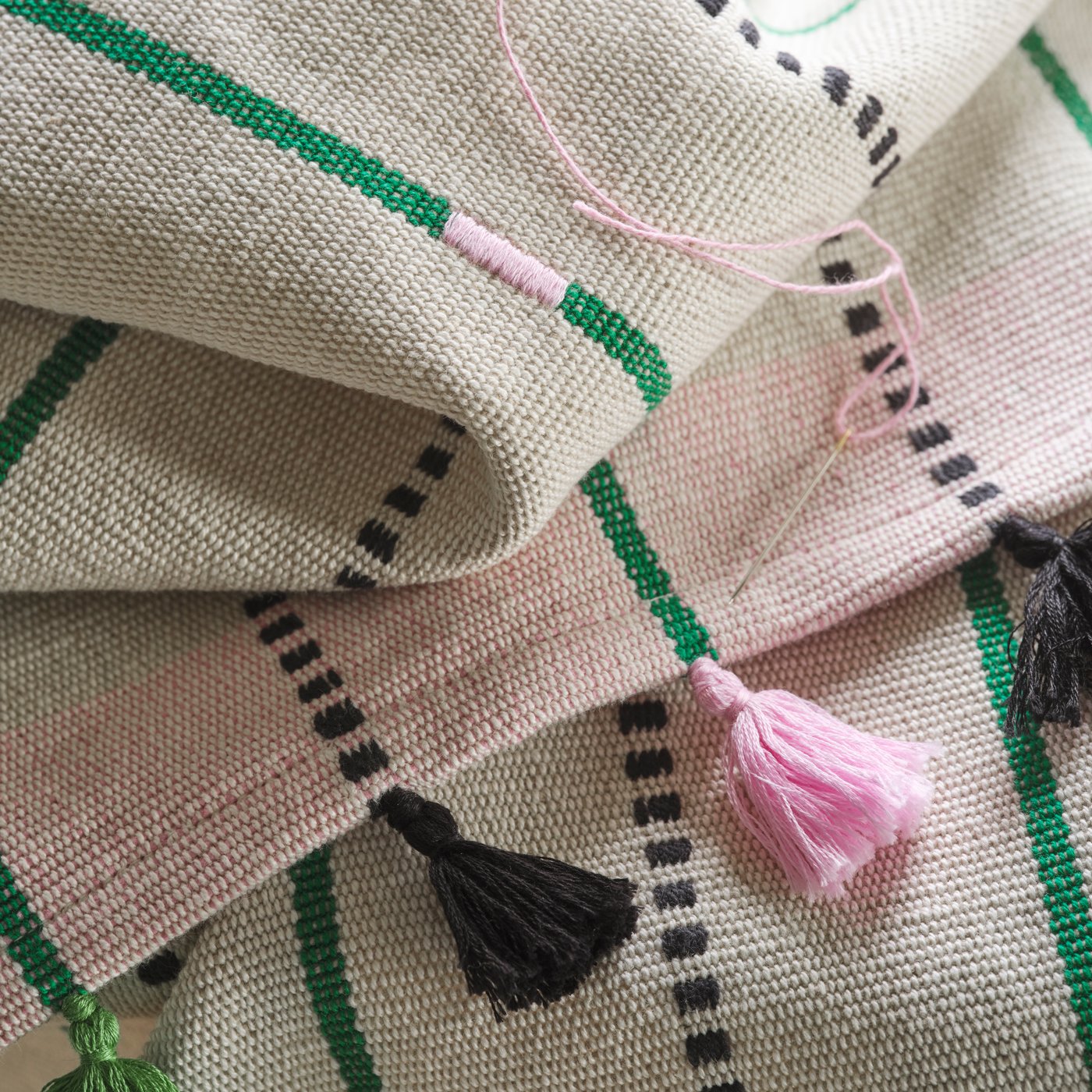 Primer plano de las tachuelas negras y rosas de un camino de mesa MÄVINN de rayas hecho a mano. Encima, hay una aguja con hilo rosa.