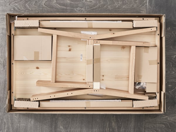 An IKEA flatpack with the top removed revealing a pine chair waiting to be assembled.