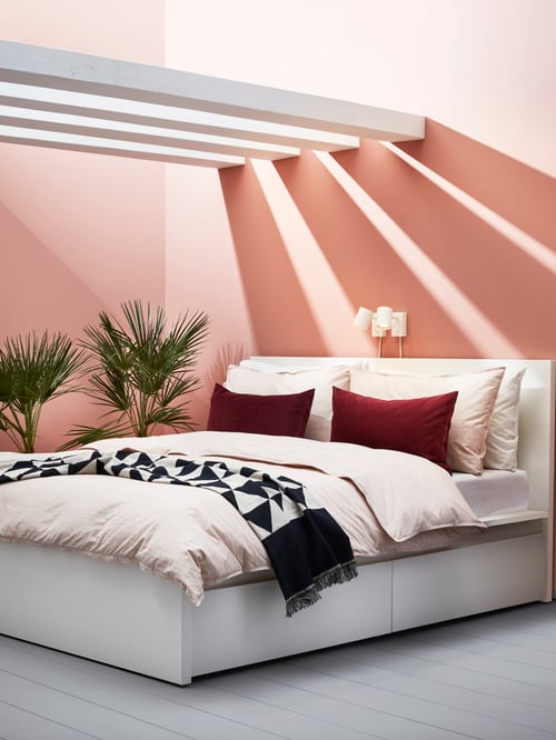 Modern bedroom with white bed frame covered with quilt cover, pillowcases and a throw next to wall reading lamp.