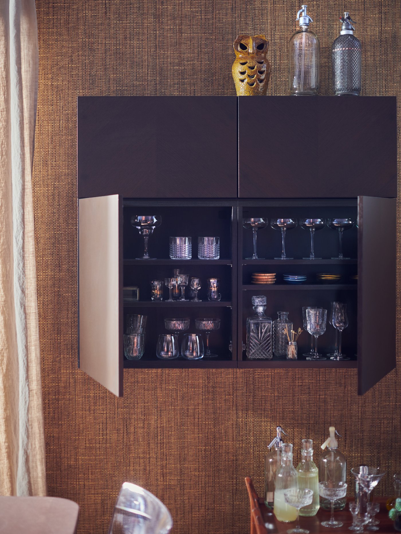 Un mueble de pared BESTÅ con puertas HEDEVIKEN. Dos puertas abiertas con vasos, posavasos y accesorios para hacer tragos.