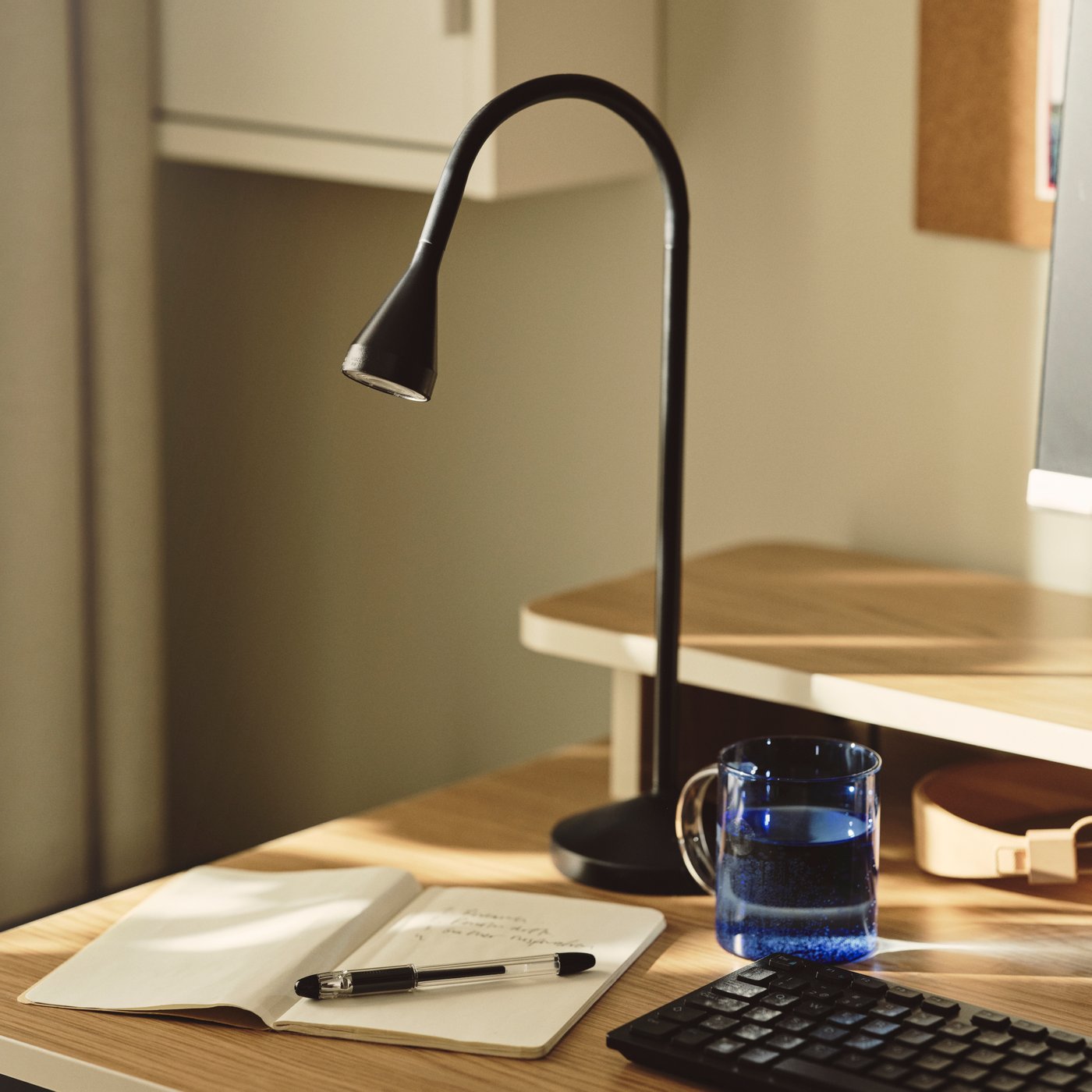 Close-up of a NÄVLINGE work lamp with a notebook and pen.