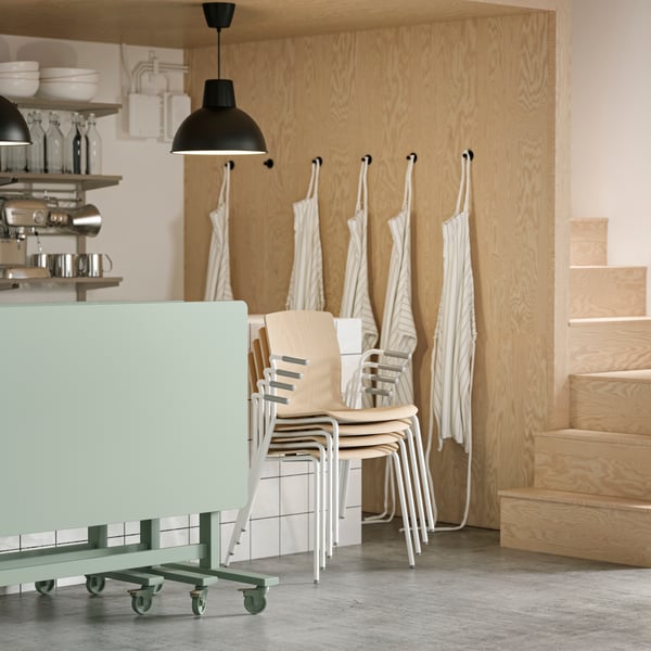 Four LÄKTARE conference chairs in birch veneer/white stacked against a counter, with green folded MITTZON tables beside them.