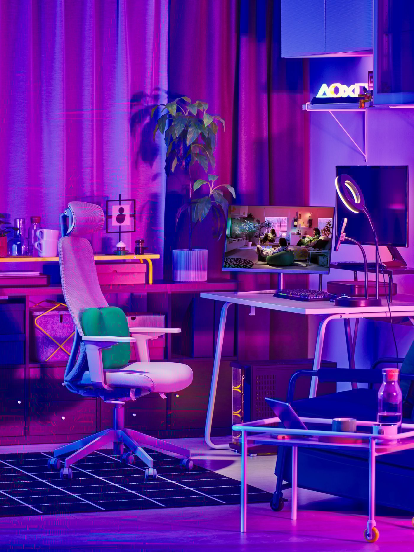 Coin gaming avec bureau IKEA, chaise ergonomique et beaucoup de déco colorée et de plantes dans une ambiance lumineuse violette.