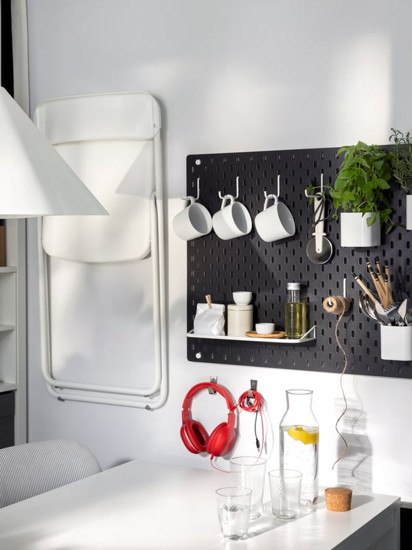 Two black SKÅDIS pegboards and a folded VIHALS folding chair are hung on a wall near a white VIHALS extendable table.