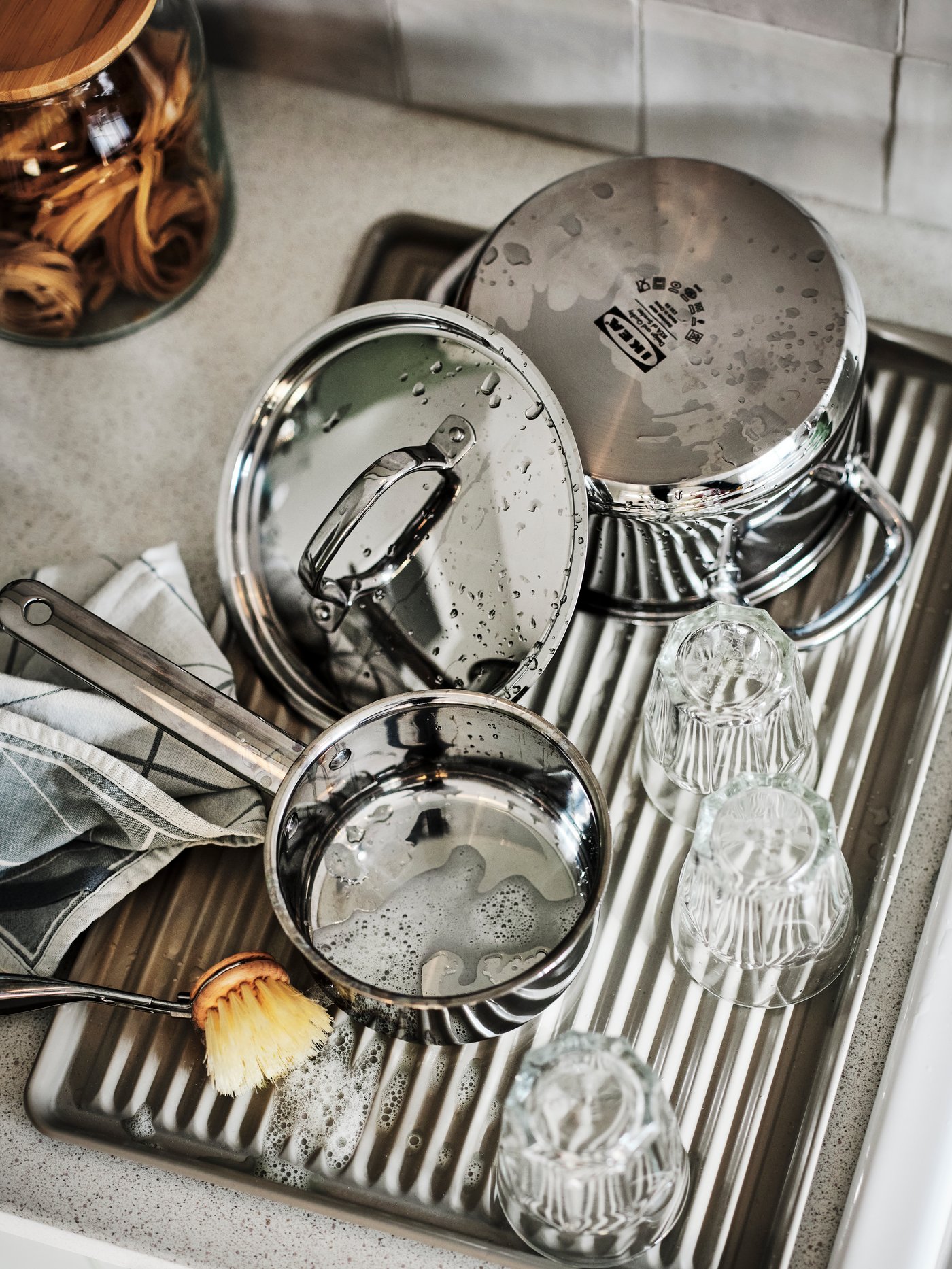 Cocina con un seca platos beige de acero galvanizado que soporta una olla, una olla con tapa y varios vasos.