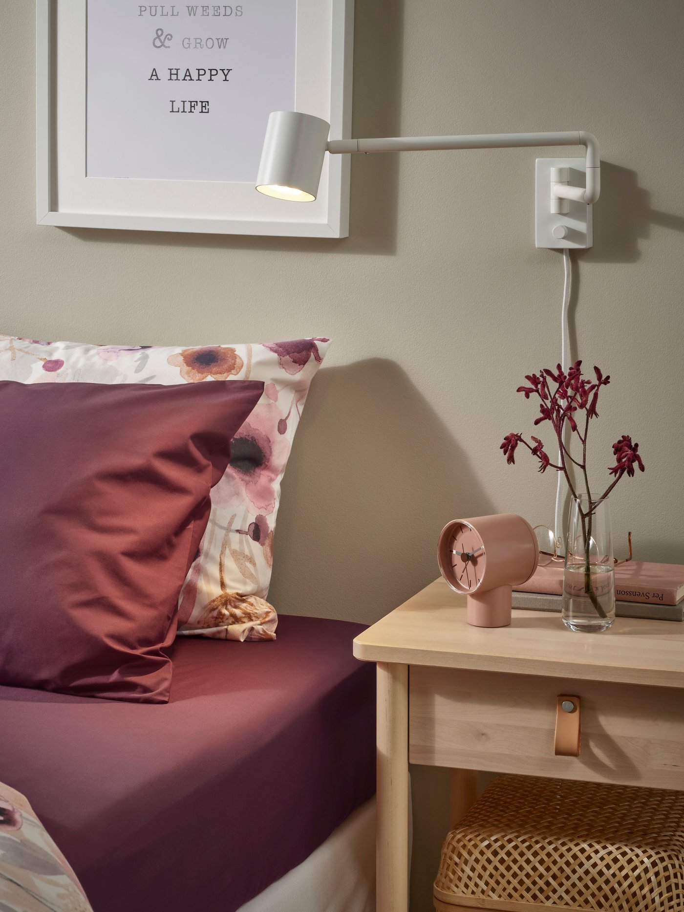 Dettaglio di una camera da letto con un letto e un comodino in legno. Sopra il comodino c'è una lampada a parete.